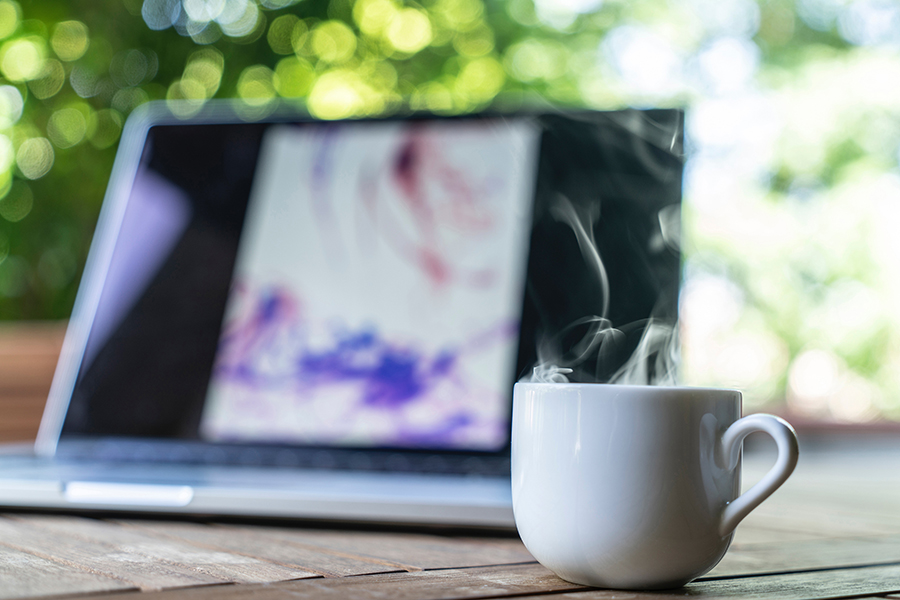 steaming cup of coffee on table in front of open laptop