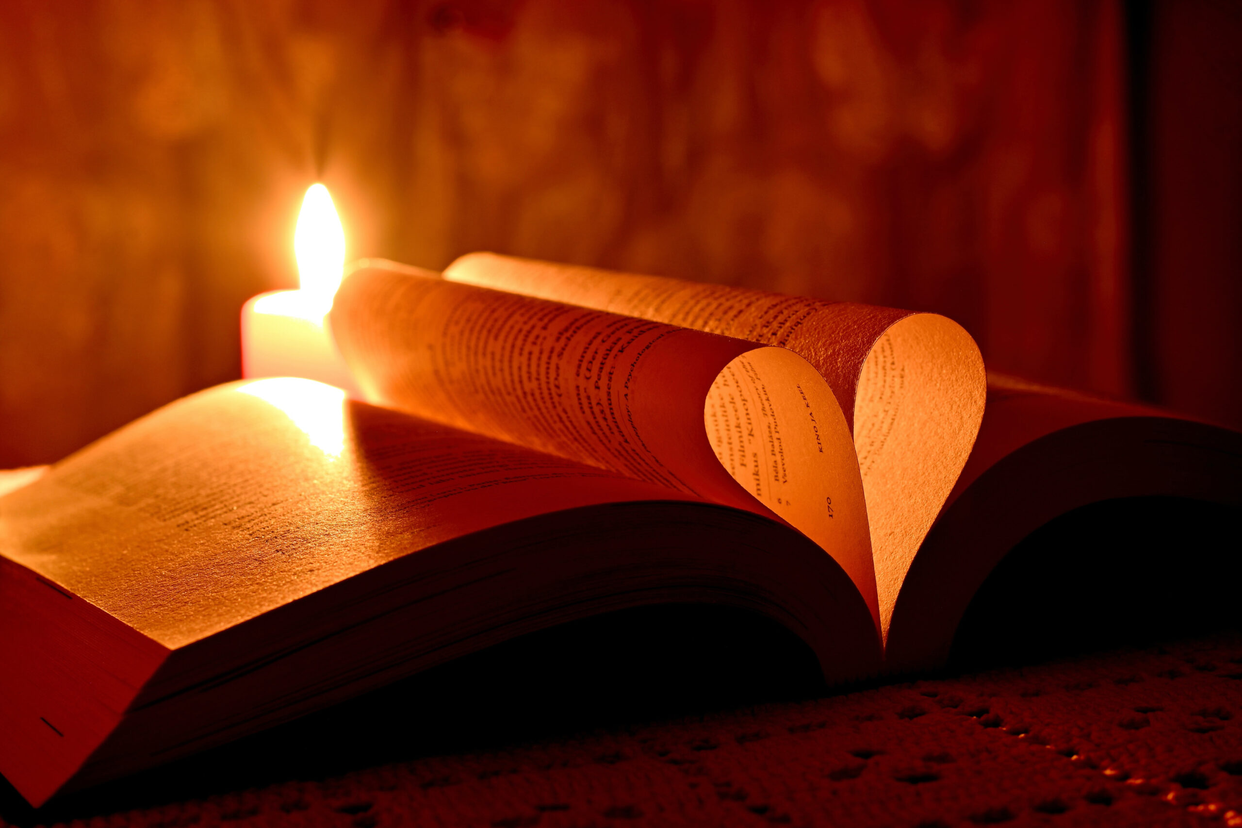 lit candle behind a bible with pages foled to make a heart shape
