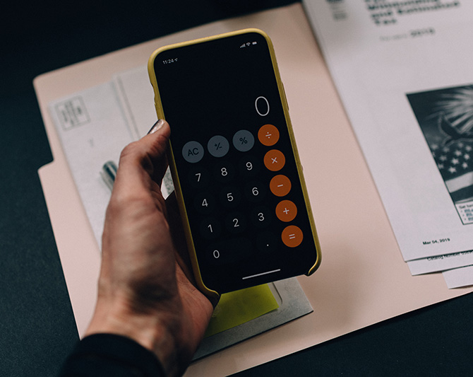 hand holding a calculator with file folder on a table behind it