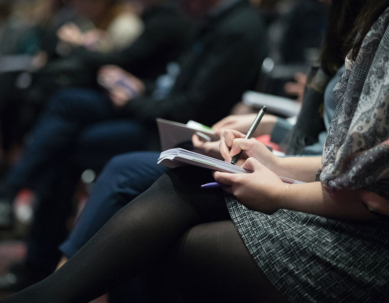 people sitting in an audience taking notes