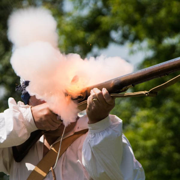 Image of a man shooting an old style musket, the smoke from the gun hides the man's face